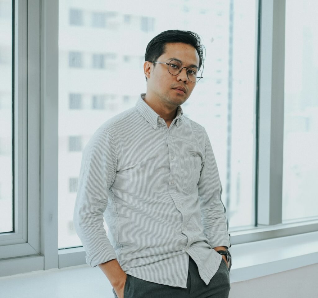 A man standing in front of a window with his hands in his pockets